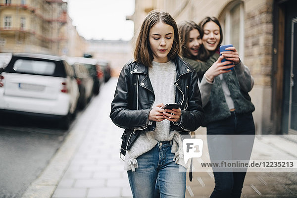 Weibliche Freunde beim Gehen auf dem Bürgersteig in der Stadt per Handy