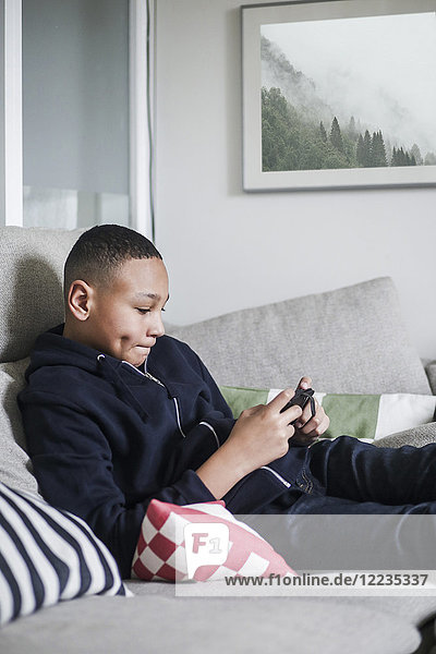 Teenager-Junge mit Handy auf Sofa im Wohnzimmer