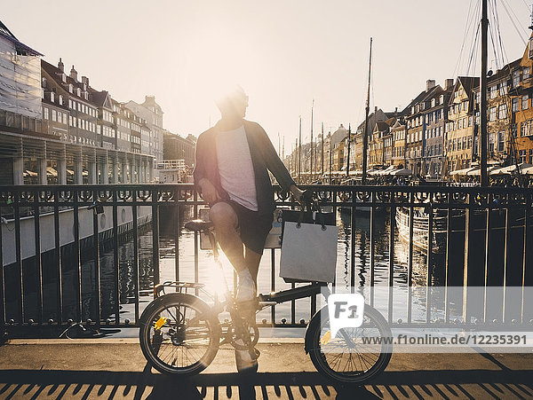 Volle Länge hinterleuchtet von Mann stehend mit Fahrrad und Einkaufstaschen auf Fußgängerbrücke in der Stadt