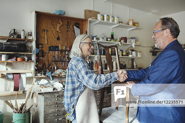 Senior Besitzer schüttelt dem Kunden beim Verkauf von Holzstühlen in der Werkstatt die Hand.