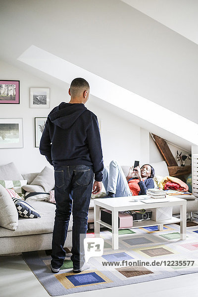 Mother photographing son on mobile phone in living room at home