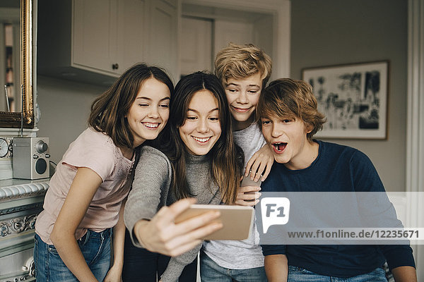Fröhliche Freunde nehmen Selfie durch Smartphone während sie zu Hause stehen.