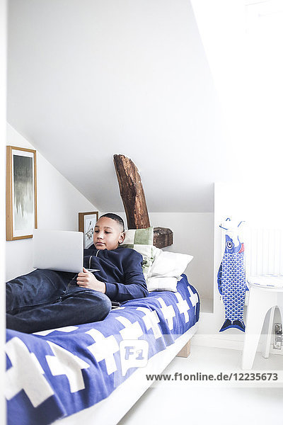 Teenager Junge mit Laptop im Bett zu Hause liegend