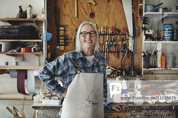 Portrait of smiling senior owner standing against tools at workshop