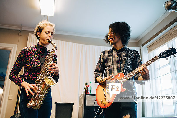 Freunde die Saxophon und Gitarre spielen während sie im Aufnahmestudio üben.
