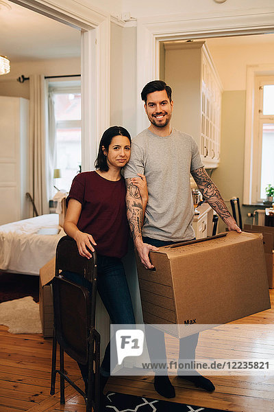 Portrait of smiling couple standing with box by rooms at home