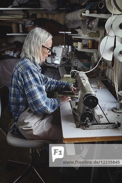 Senior owner using sewing machine at workshop