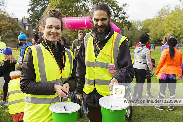 Portrait smiling volunteers with donation buckets at charity run in park