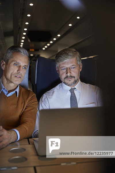 Businessmen working at laptop on passenger train at night