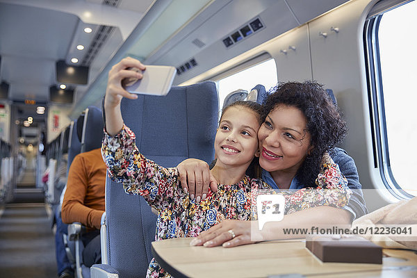 Affectionate mother and daughter taking selfie with camera phone on passenger train
