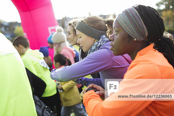 Focused female runners with smart watches poised  ready at charity run starting line
