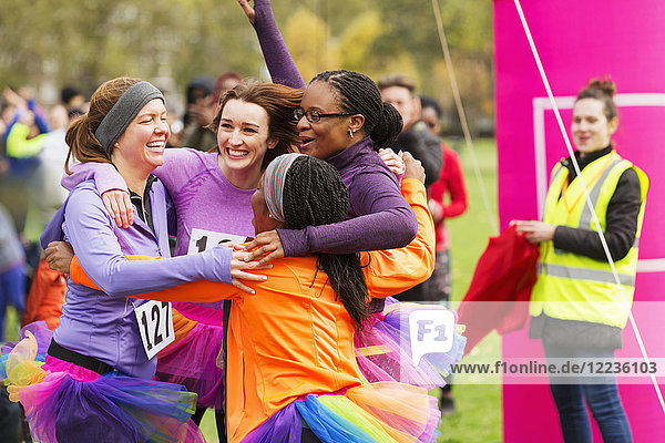 Enthusiastic female runners in tutus hugging at finish line  celebrating