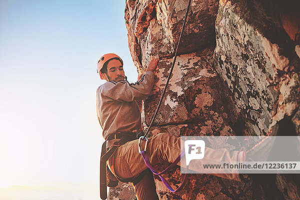 Fokussierter männlicher Kletterer am Fels hängend