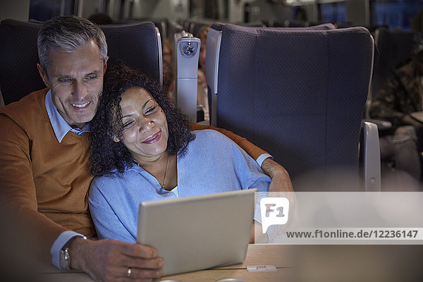 Liebevolles Paar  das sich nachts einen Film auf einem digitalen Tablett im Personenzug ansieht.