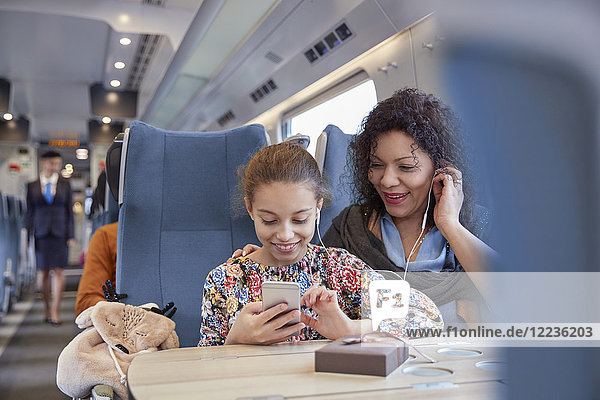 Mutter und Tochter teilen sich Kopfhörer  Musik hören mit Smartphone im Personenzug