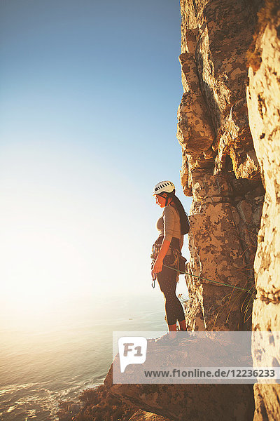 Female rock climber looking at sunny ocean view