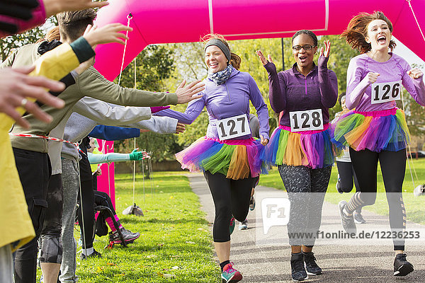 Spectators high-fiving female runners in tutus crossing charity run finish line
