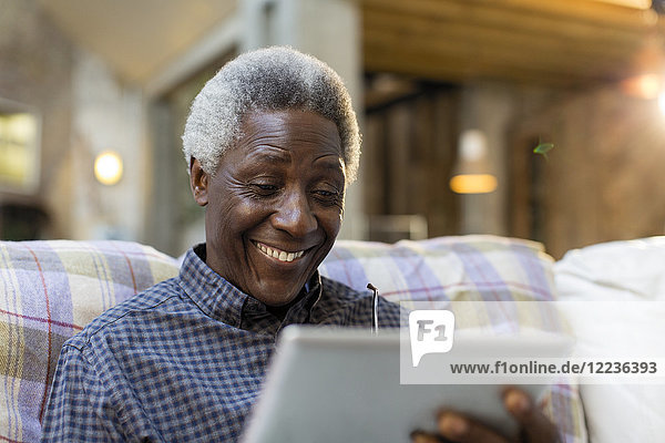 Lächelnder älterer Mann mit digitalem Tablett auf dem Sofa