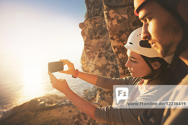 Rock climbers with camera phone photographing ocean view