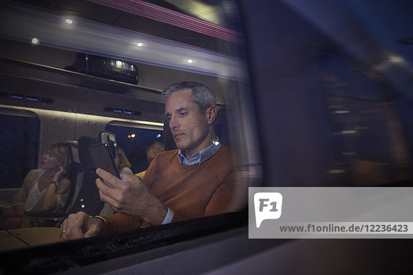 Geschäftsmann mit Smartphone am Fenster im Personenzug bei Nacht
