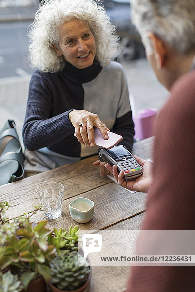 Frau mit Smartphone kontaktlos bezahlen im Cafe