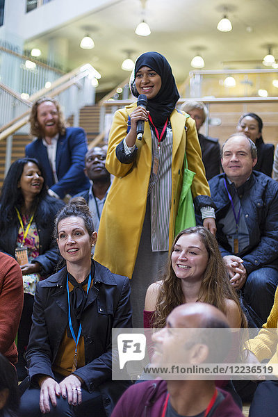 Lächelnde Frau im Hijab im Gespräch mit Mikrofon im Konferenzpublikum