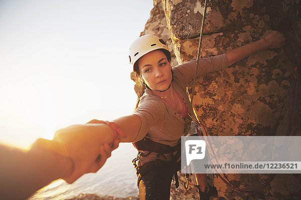 Focused female rock climber reaching for arm
