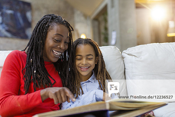 Smiling mother and daughter looking at photo album on sofa
