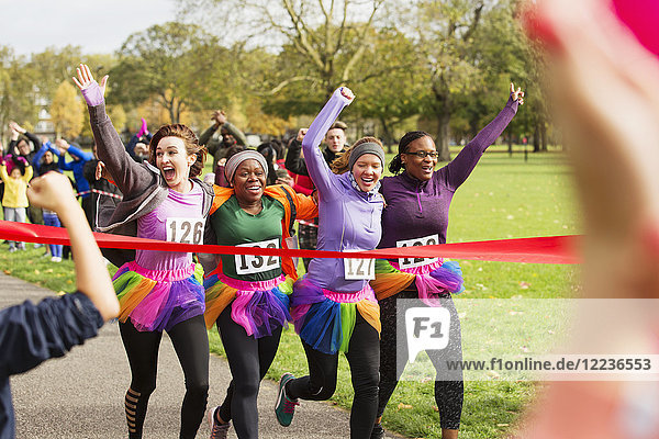 Enthusiastic female runners in tutus crossing charity run finish line in park  celebrating
