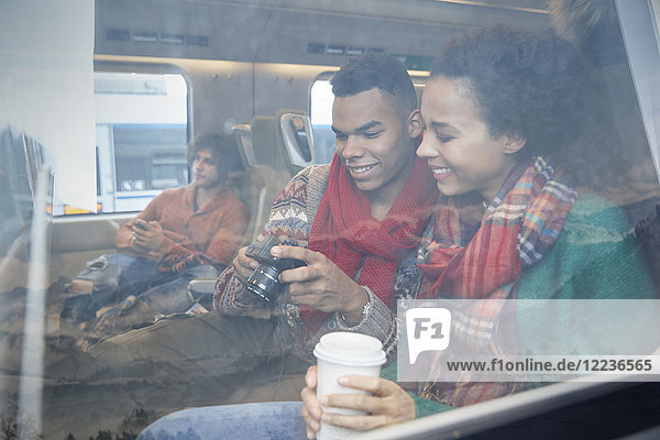 Junges Paar mit Kaffee beim Blick auf die Digitalkamera am Fenster des Personenzuges