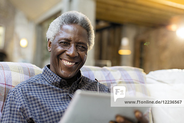 Portrait lächelnder  selbstbewusster Senior mit digitalem Tablett auf dem Sofa
