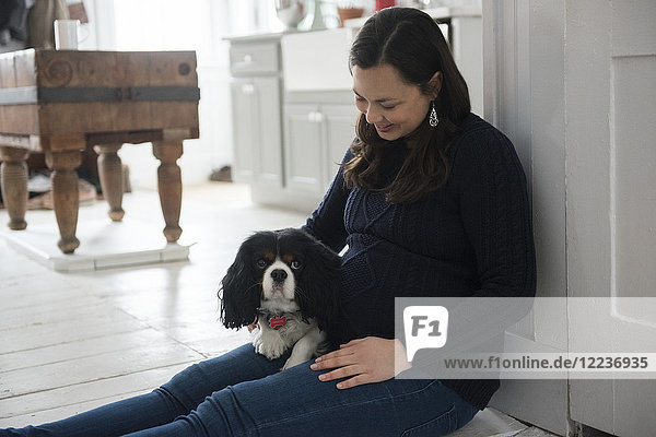 Schwangere Frau sitzt auf dem Boden und hält einen Hund