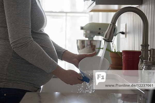 Pregnant woman washing bowl in kitchen sink  mid section