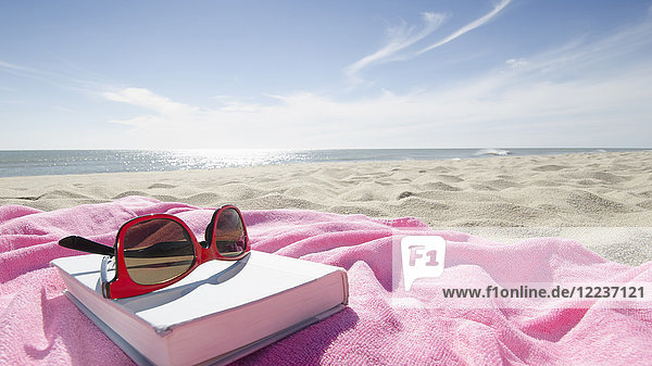 Buch und Sonnenbrille auf rosa Handtuch am Sandstrand