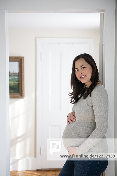 Porträt einer schwangeren Frau  die in der Tür steht und ihren Bauch berührt