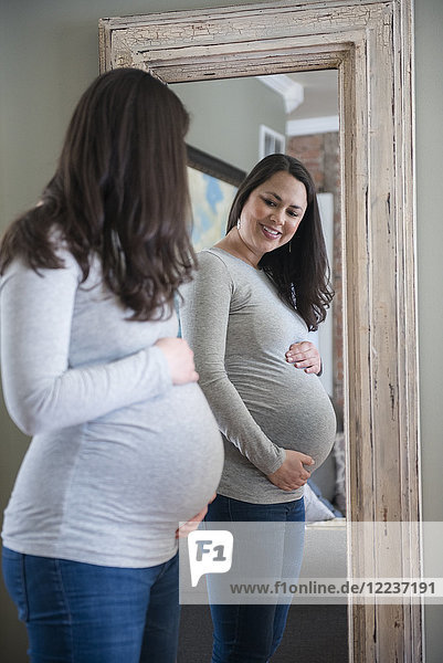 Schwangere Frau schaut in den Spiegel und berührt ihren Bauch
