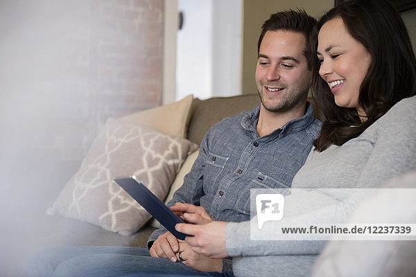 Mid adult couple sitting on sofa and using tablet pc