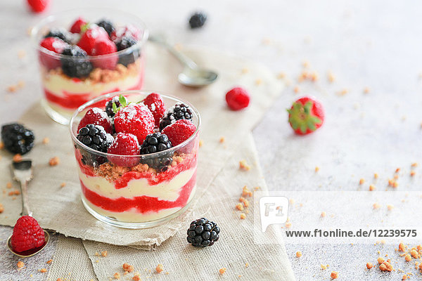 Geschichtete Desserts in Gläsern mit Puddingcreme  Fruchtsauce  Kekskrümeln und Beeren