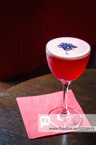 Roter Cocktail mit Kornblumen dekoriert auf roter Serviette und Holztisch