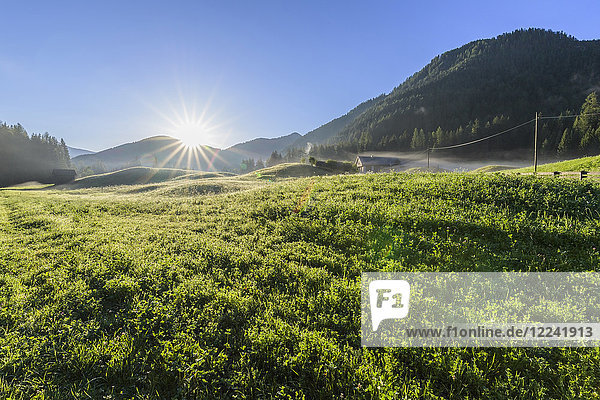 Morgensonne über einer nebligen Bergwiese in den Pragser Dolomiten in der Provinz Bozen (Südtirol)  Italien