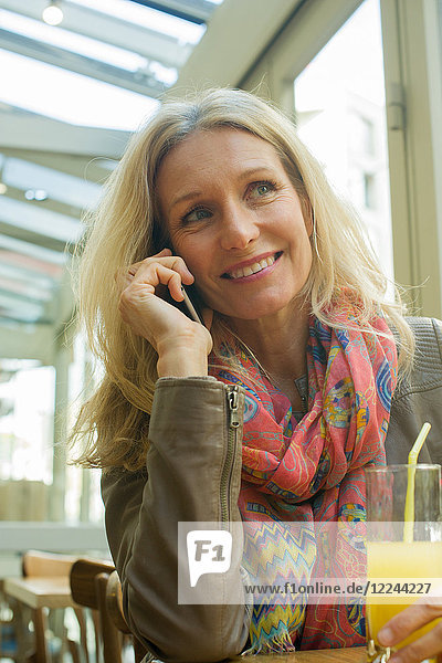 Reife Frau spricht am Handy und lächelt im Cafe