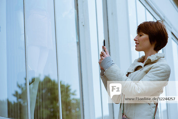 Frau fotografiert Schaufenster mit Smartphone