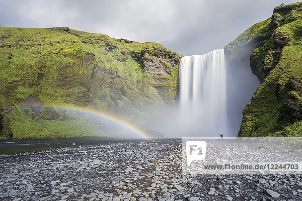 Doppelter Regenbogen und Touristen mit Händen in der Luft am Skogafoss-Wasserfall in Südisland  Polarregionen