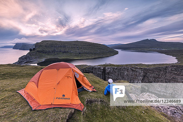 Camping tent and hiker on cliff above lake Sorvagsvatn at sunset  Vagar Island  Faroe Islands  Denmark  Europe