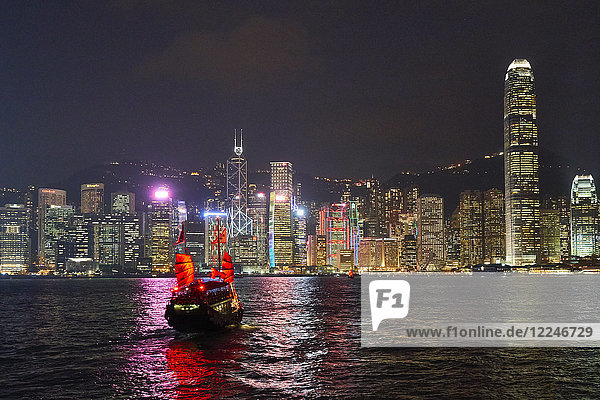 Traditional junk boat on Victoria Harbour with city skyline behind illuminated at night  Hong Kong  China  Asia