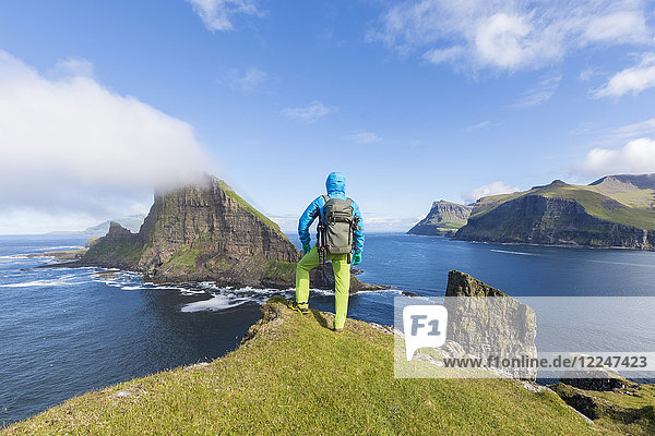 Man looks towards the sea stacks of Drangarnir and Tindholmur islet Vagar Island Faroe Islands Denmark Europe