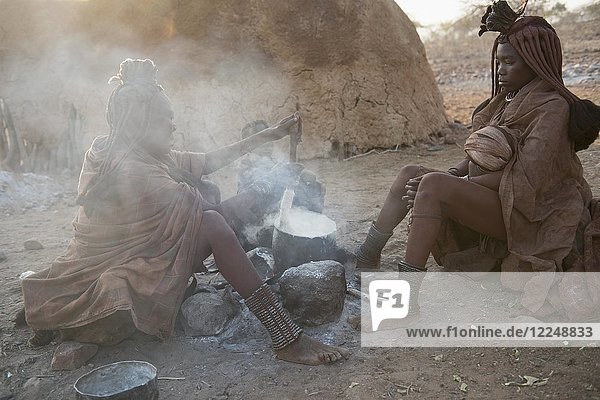 Two hang-girls cooking in front of a mud hut by the fire  Kaokoveld  Kunene  Namibia  Africa