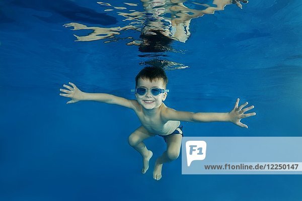 Kleiner Junge mit Schwimmbrille taucht in einen Pool
