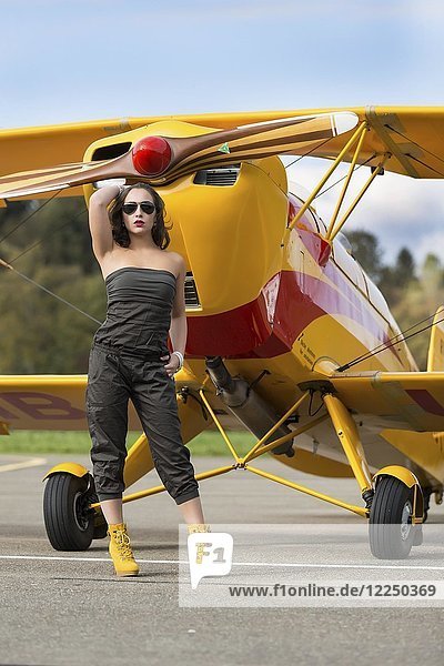 Junge Frau mit Sonnenbrille in Overall und Stiefeln posiert vor einem Doppeldecker-Flugzeug  Mode  Lifestyle  Fotoshooting
