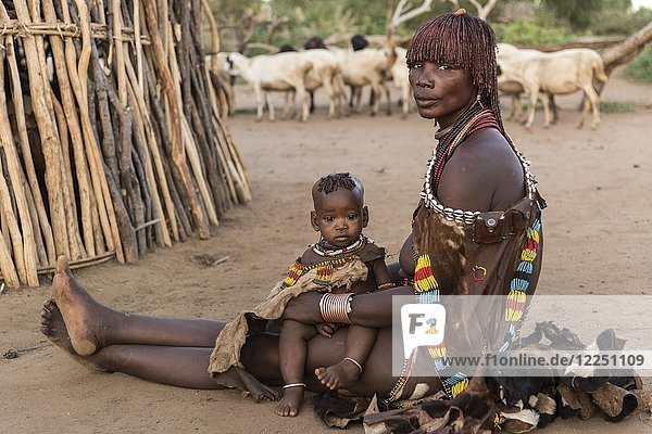 Frau mit Kleinkind vor einer Lehmhütte auf dem Boden sitzend  Stamm der Hamer  Turmi  Region der südlichen Nationen  Äthiopien  Afrika